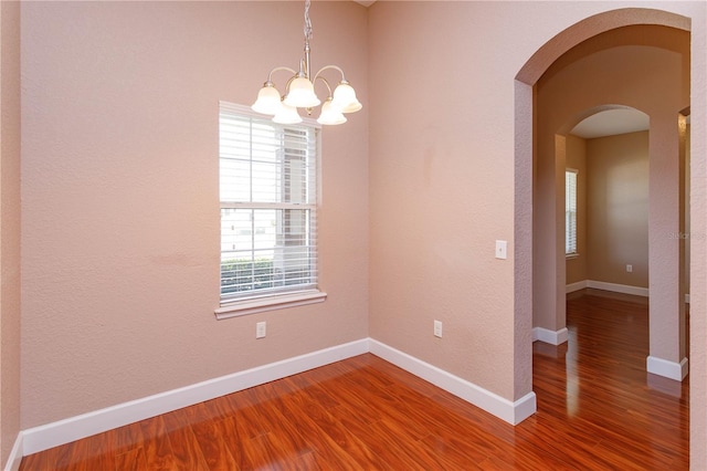 spare room with baseboards, wood finished floors, arched walkways, and a notable chandelier