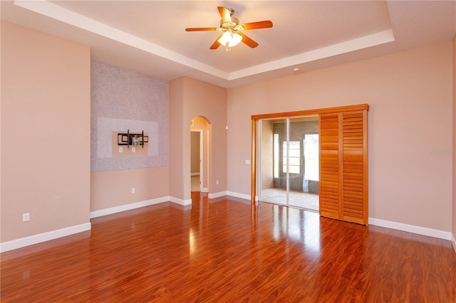 unfurnished bedroom featuring arched walkways, wood finished floors, baseboards, and a tray ceiling