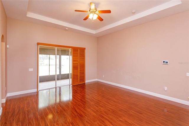 empty room featuring baseboards, a ceiling fan, wood finished floors, and a raised ceiling