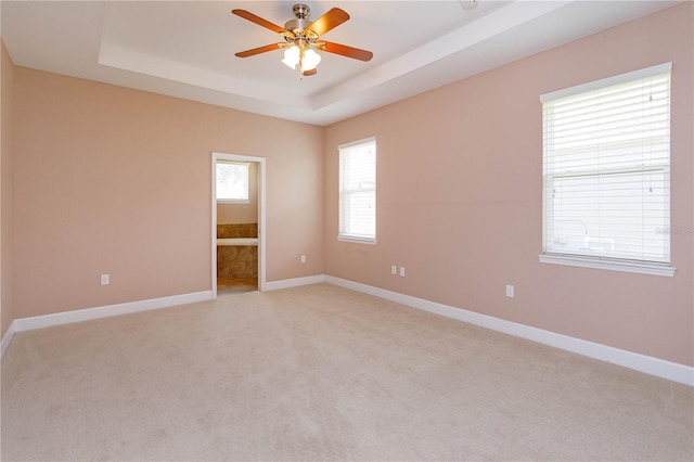 spare room with ceiling fan, baseboards, a tray ceiling, and light colored carpet
