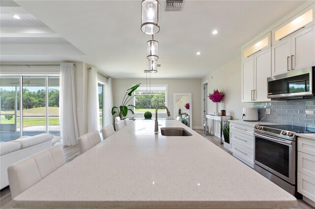 kitchen featuring backsplash, visible vents, appliances with stainless steel finishes, a sink, and an island with sink