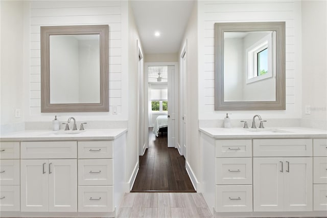 ensuite bathroom with baseboards, two vanities, a sink, and wood finished floors