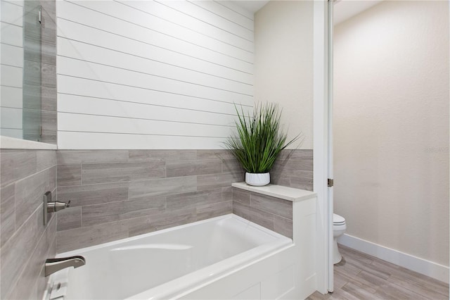 bathroom featuring baseboards, a bath, wood finished floors, and toilet