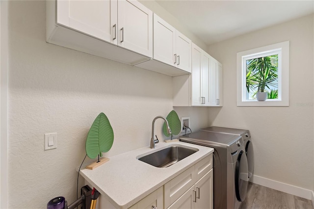 washroom with baseboards, light wood-style flooring, separate washer and dryer, a sink, and cabinet space