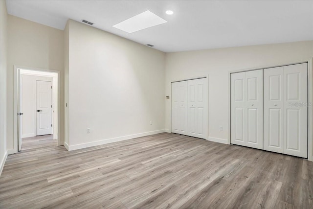 unfurnished bedroom with a skylight, multiple closets, baseboards, and light wood finished floors