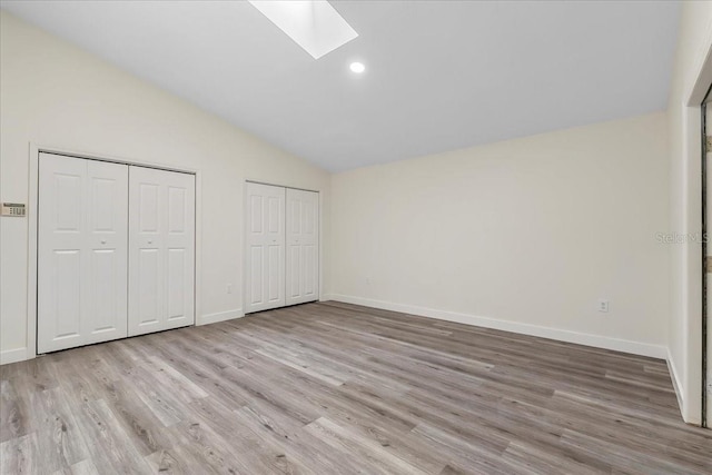 unfurnished bedroom featuring multiple closets, baseboards, light wood finished floors, and lofted ceiling with skylight