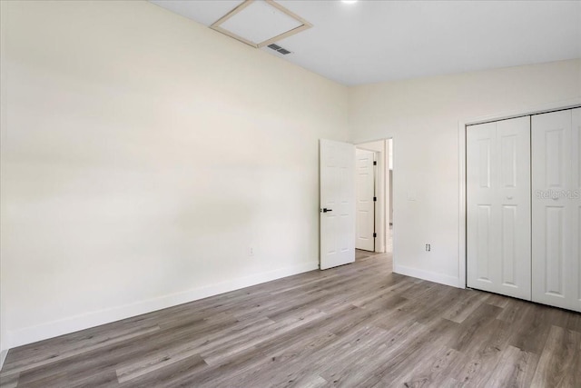 unfurnished bedroom featuring visible vents, a closet, wood finished floors, baseboards, and attic access