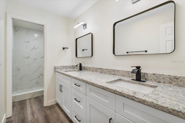 full bathroom with a sink, a marble finish shower, double vanity, and wood finished floors