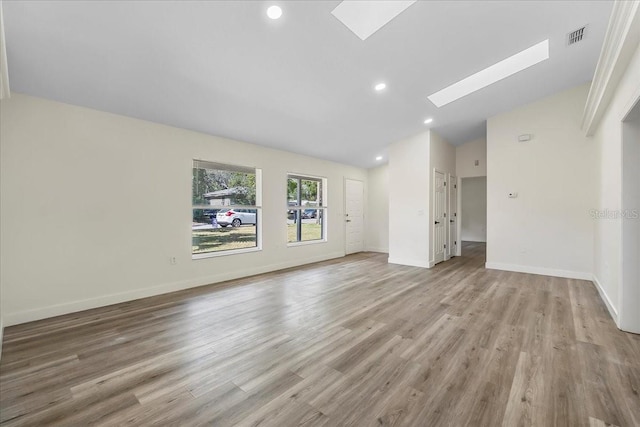 spare room with visible vents, light wood finished floors, lofted ceiling with skylight, and baseboards