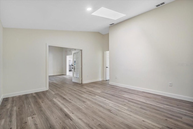 empty room with baseboards, visible vents, wood finished floors, and lofted ceiling with skylight