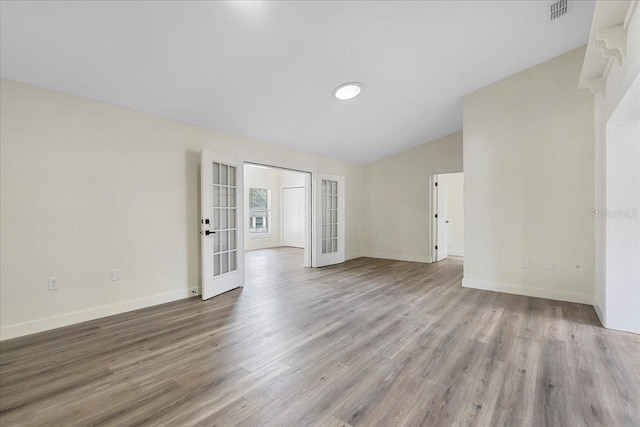 unfurnished room featuring visible vents, wood finished floors, baseboards, french doors, and vaulted ceiling