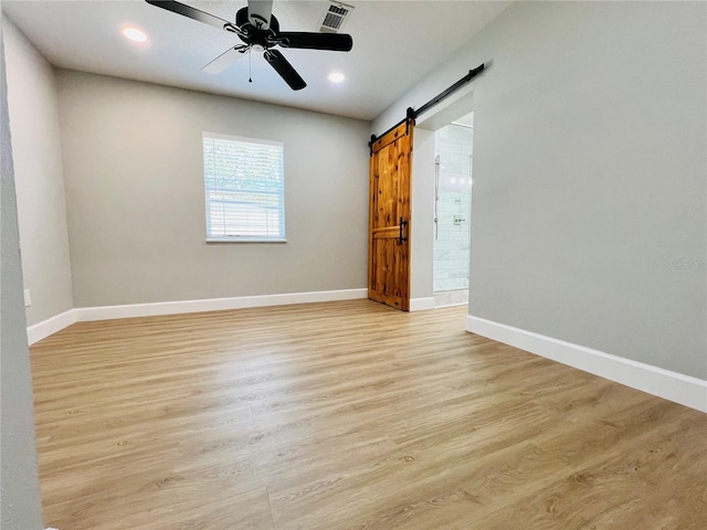 spare room featuring a barn door, a ceiling fan, visible vents, light wood-style flooring, and baseboards