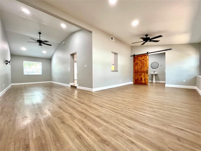 unfurnished living room featuring light wood-type flooring, a barn door, and a ceiling fan