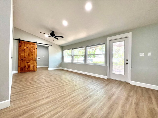 unfurnished living room featuring light wood-style flooring, a barn door, vaulted ceiling, baseboards, and a ceiling fan