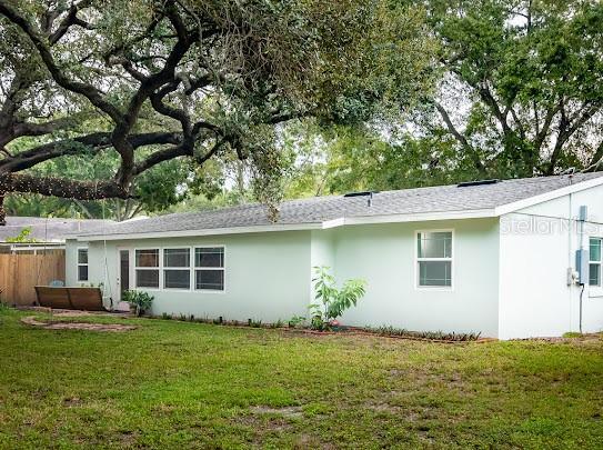 rear view of property featuring a lawn, stucco siding, and fence