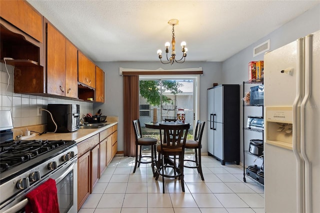 kitchen with visible vents, stainless steel gas range, brown cabinets, a notable chandelier, and white fridge with ice dispenser