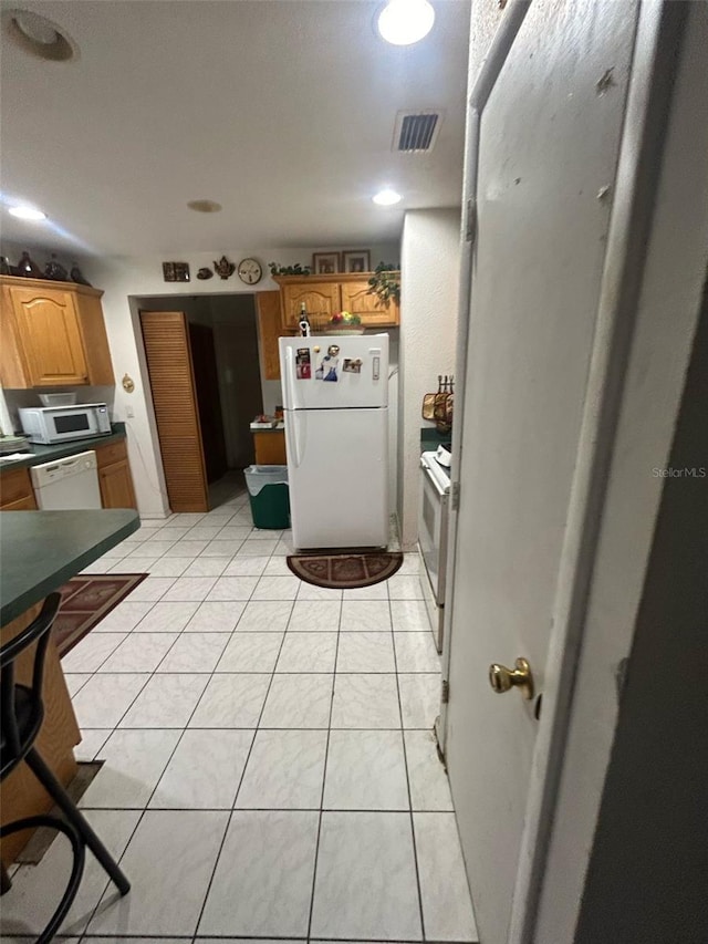 kitchen with light tile patterned floors, dark countertops, visible vents, white appliances, and brown cabinetry