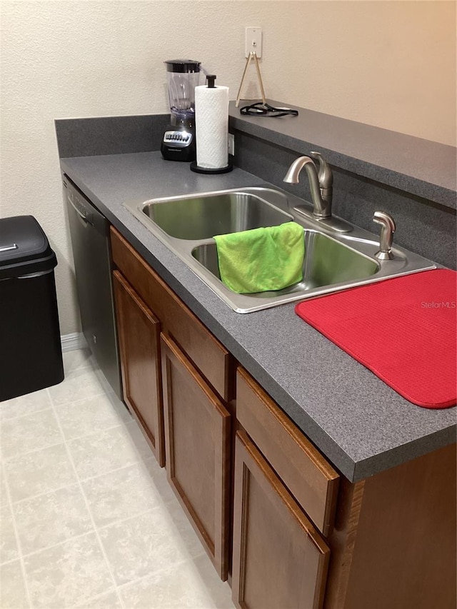 kitchen featuring brown cabinets, dark countertops, a sink, dishwasher, and light tile patterned floors