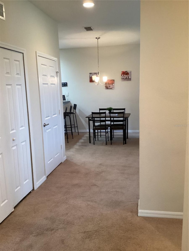 hallway featuring visible vents, carpet, baseboards, and an inviting chandelier
