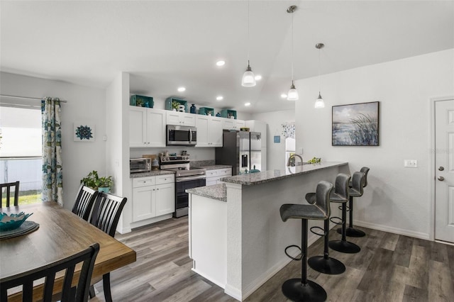 kitchen featuring a kitchen breakfast bar, appliances with stainless steel finishes, dark wood finished floors, a peninsula, and white cabinetry