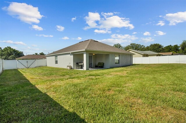back of house with a patio area, a fenced backyard, a yard, a shingled roof, and stucco siding