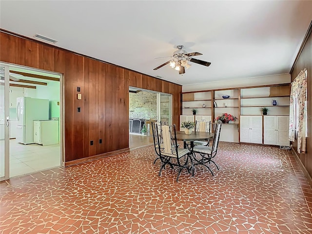 dining space with visible vents, ornamental molding, ceiling fan, wooden walls, and stone finish flooring