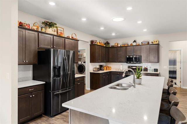 kitchen featuring dark brown cabinetry, appliances with stainless steel finishes, light wood-type flooring, a sink, and a breakfast bar