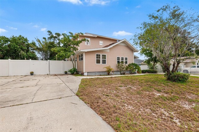 view of side of property with a lawn, a gate, fence, and concrete driveway