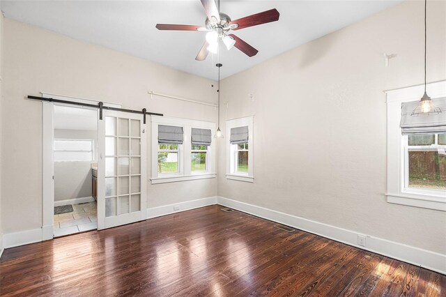 spare room with baseboards, a barn door, ceiling fan, and wood finished floors