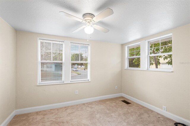 empty room with visible vents, carpet floors, baseboards, a textured ceiling, and a ceiling fan