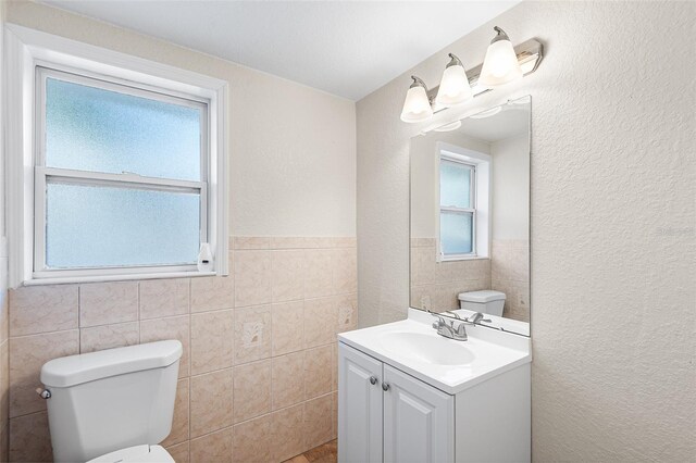 bathroom with vanity, a wainscoted wall, toilet, and tile walls