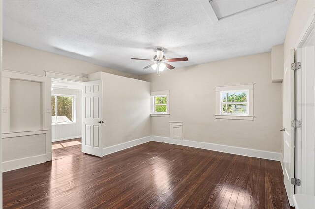 spare room featuring baseboards, attic access, a textured ceiling, a ceiling fan, and dark wood finished floors