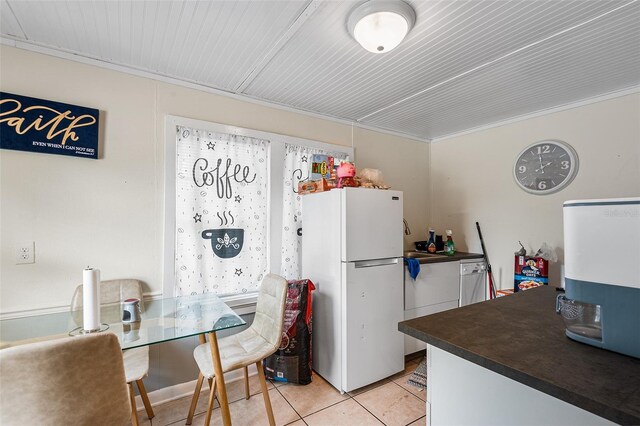 kitchen with light tile patterned floors, dark countertops, freestanding refrigerator, and a sink