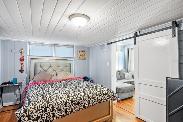bedroom featuring wooden ceiling, visible vents, a barn door, and wood finished floors