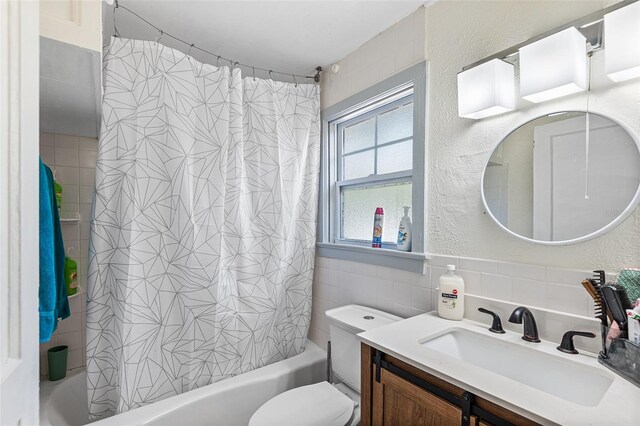 full bath with vanity, a textured wall, tile walls, and shower / tub combo