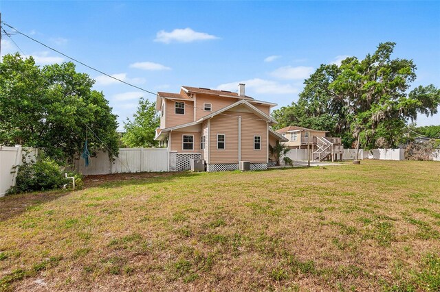 rear view of house featuring a lawn, a fenced backyard, a chimney, and cooling unit