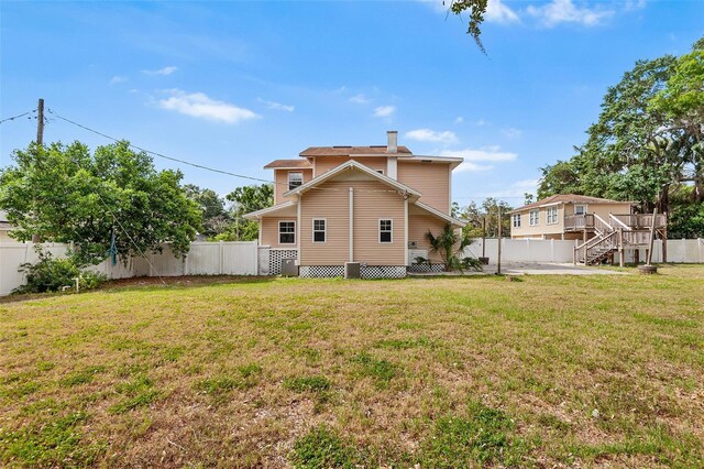 back of property with a yard, a chimney, a fenced backyard, and stairs