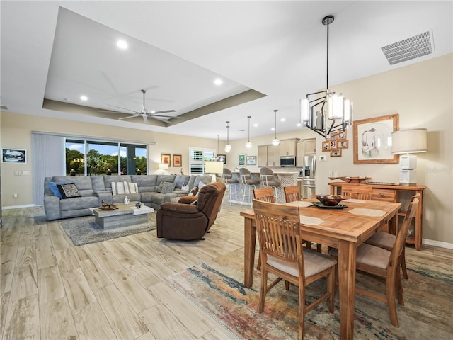 dining space featuring visible vents, a raised ceiling, light wood finished floors, and baseboards