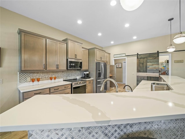 kitchen featuring hanging light fixtures, a barn door, light stone counters, stainless steel appliances, and tasteful backsplash