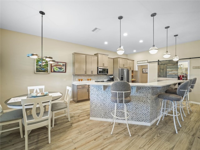 kitchen featuring a barn door, a kitchen breakfast bar, light wood-style flooring, stainless steel appliances, and visible vents