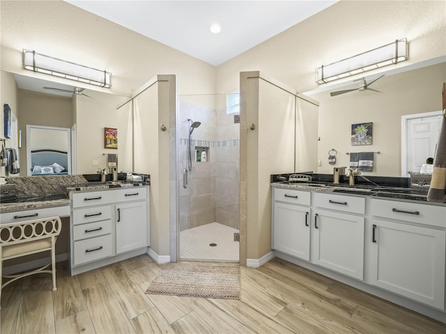 full bath featuring a ceiling fan, a shower stall, wood finished floors, two vanities, and lofted ceiling