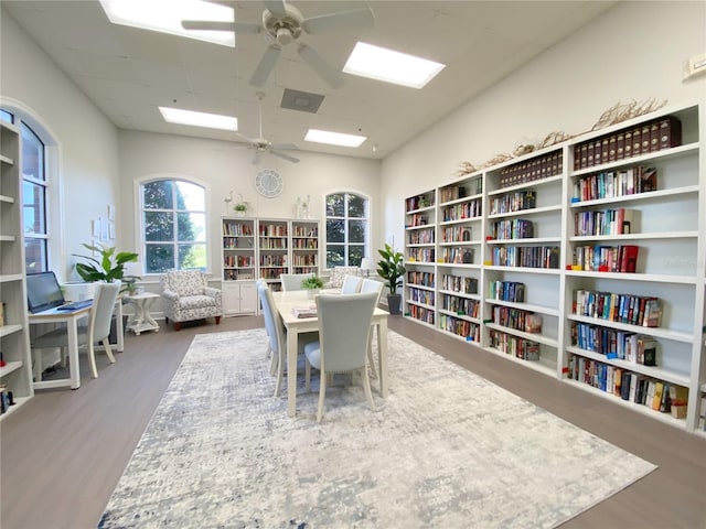 sitting room with ceiling fan, wall of books, and wood finished floors