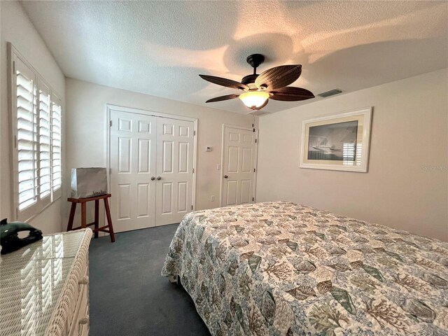 bedroom with visible vents, a textured ceiling, dark carpet, and a closet