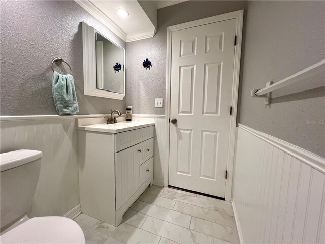 half bath with vanity, marble finish floor, a wainscoted wall, and toilet