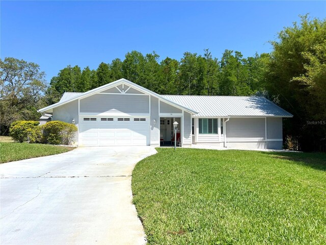 ranch-style home with an attached garage, driveway, a front yard, and metal roof