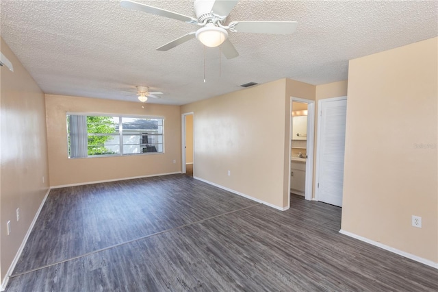 empty room with a textured ceiling, baseboards, visible vents, and dark wood-type flooring