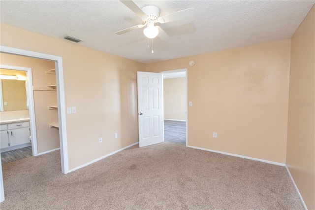 unfurnished bedroom featuring carpet floors, a textured ceiling, visible vents, and a walk in closet