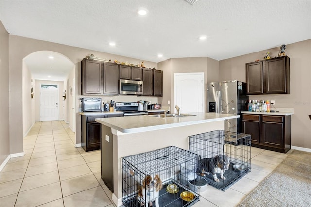 kitchen featuring stainless steel appliances, light tile patterned floors, a sink, and dark brown cabinets