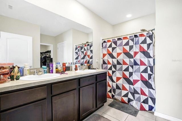 full bath with double vanity, a sink, tile patterned floors, and a spacious closet