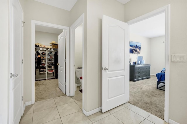hall featuring baseboards, light colored carpet, and light tile patterned floors